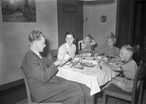 803548 Afbeelding van een gezin aan de ontbijttafel in een huis te Rijswijk, met links de vader die een reis opzoekt in ...